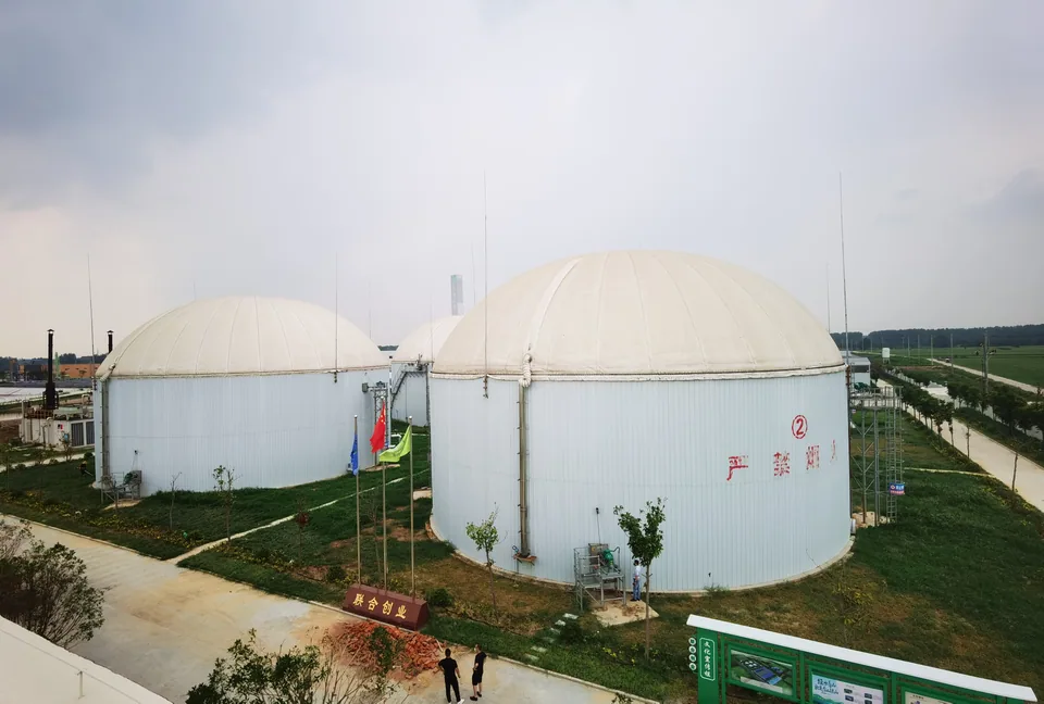 Biogas plant with multiple membrane-roof anaerobic digesters, power-generation equipment, pipework platforms, and landscaped access roads