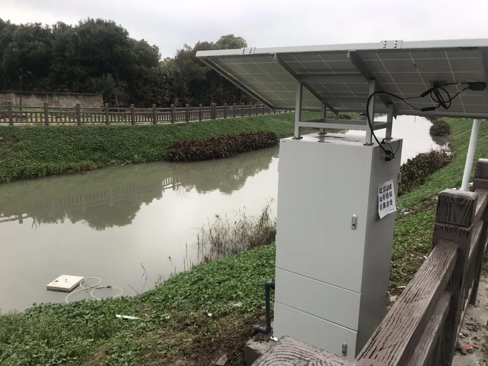Riverside water-quality monitoring station with an instrument cabinet, solar-power canopy, and surrounding river landscape